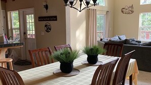 A dining area with a table set for four, surrounded by wooden chairs, a chandelier, and potted plants. - Beautiful & Cozy Cabin. Perfect Location, Kid Friendly. Free Starlink WIFI. (Cold Springs)