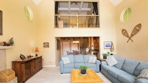A spacious living room with a high ceiling, a wooden coffee table, two sofas, a fireplace, and a dining area in the background. - Beautiful & Cozy Cabin. Perfect Location, Kid Friendly. Free Starlink WIFI. (Cold Springs)
