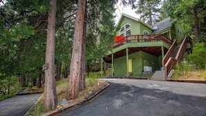 A two-story house with a green exterior, a balcony, and a staircase leading to the second floor. - Beautiful & Cozy Cabin. Perfect Location, Kid Friendly. Free Starlink WIFI. (Cold Springs)