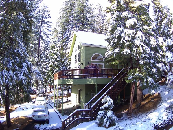 A two-story building with a balcony, surrounded by snow-covered trees. - Beautiful & Cozy Cabin. Perfect Location, Kid Friendly. Free Starlink WIFI. (Cold Springs)