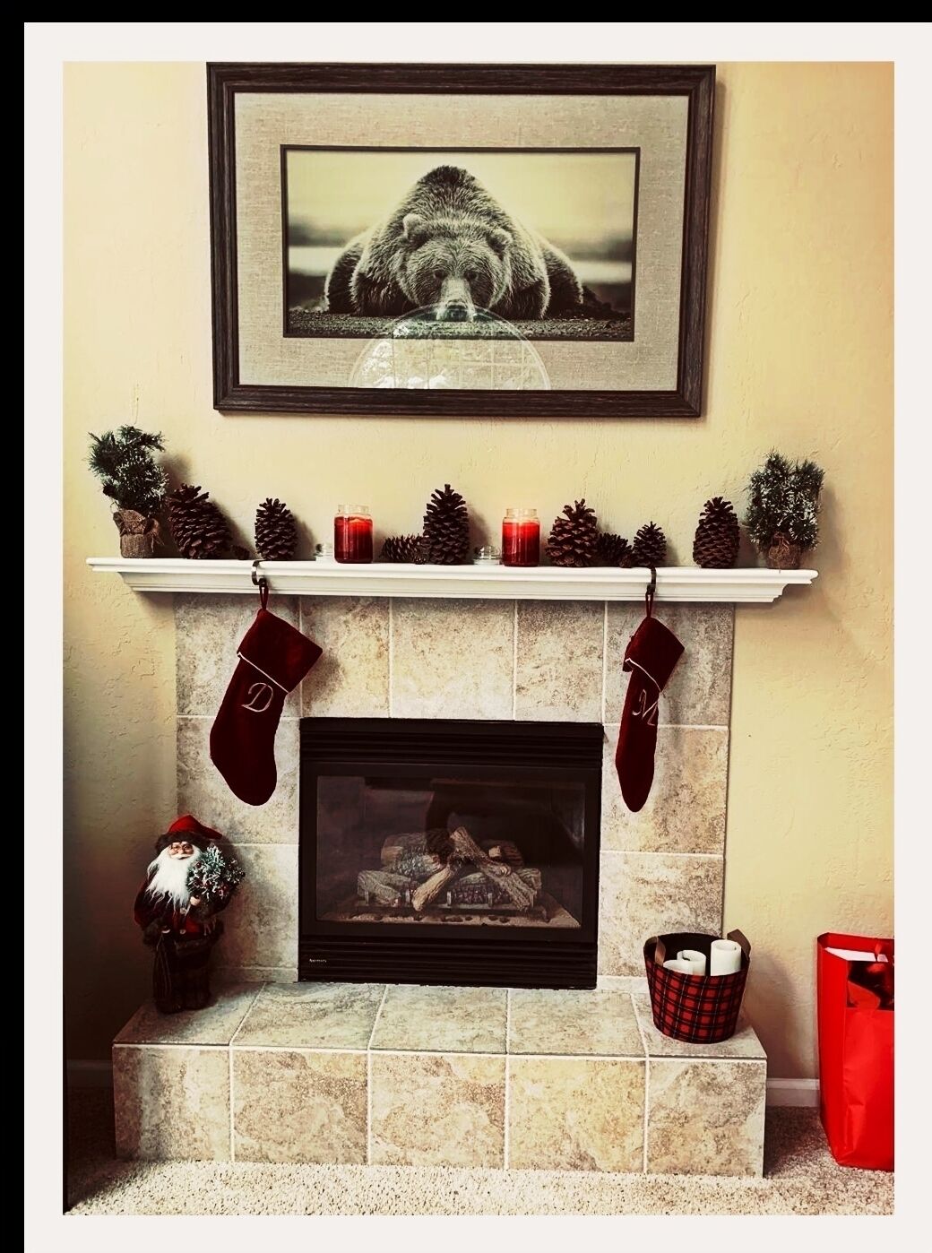 A fireplace with stockings, a framed picture above, and a small Christmas tree.