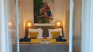 Une chambre moderne avec un lit, deux lampes fixées au mur et un tableau sur le thème des pays tropicaux.