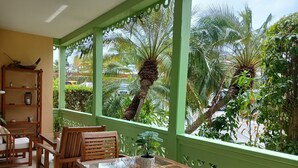 Un balcon doté de mobilier en bois, d’une table en verre et offrant une vue sur des palmiers et une végétation luxuriante.