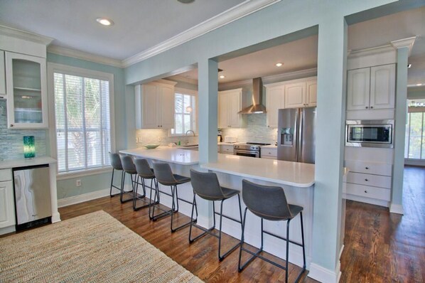 A modern kitchen with white cabinets, a central island with bar stools, stainless steel appliances, and a large window providing natural light. - It's All Good, Sleeps 12, Private Heated Pool, Steps to Beach, Fabulous Gulf Views (Santa Rosa Beach)