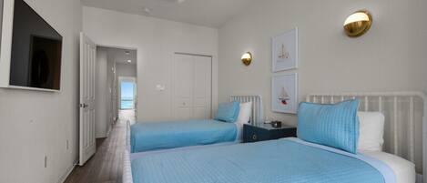 Un dormitorio con dos camas, un ventilador de techo y vista al mar a través de una puerta abierta.