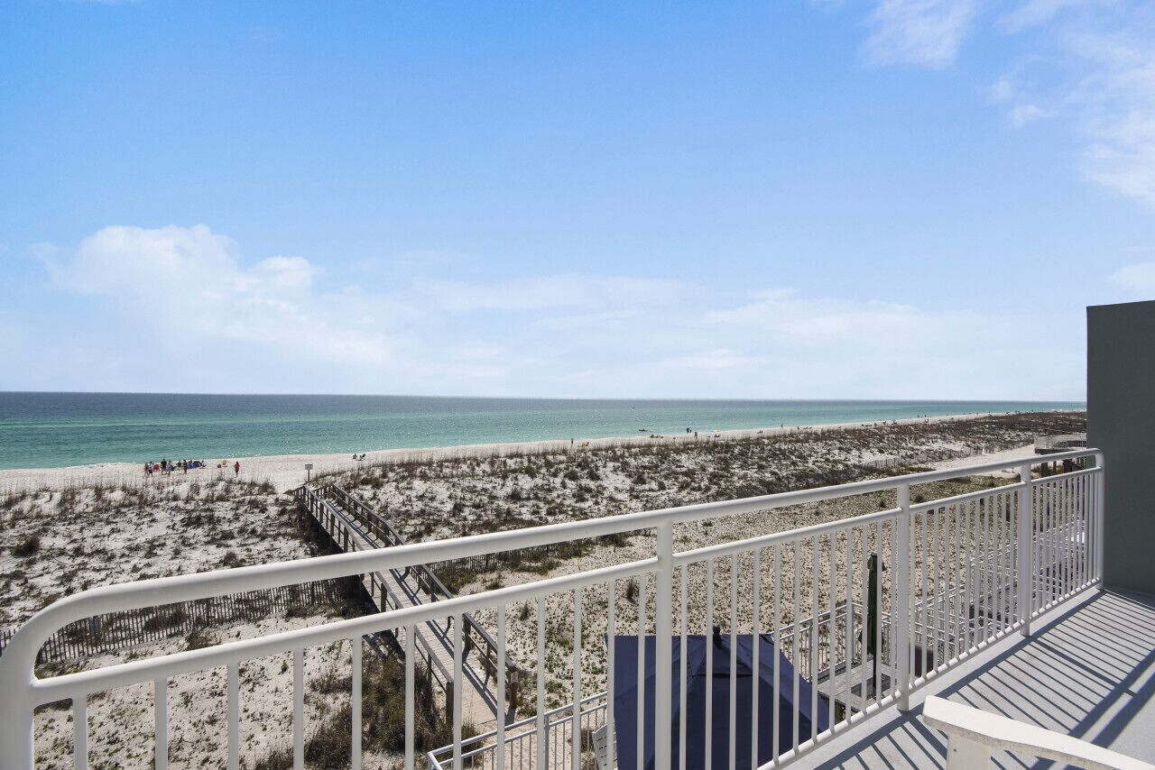 Une vue sur la plage depuis un balcon doté d’une balustrade, avec une plage de sable et l’océan en arrière-plan.