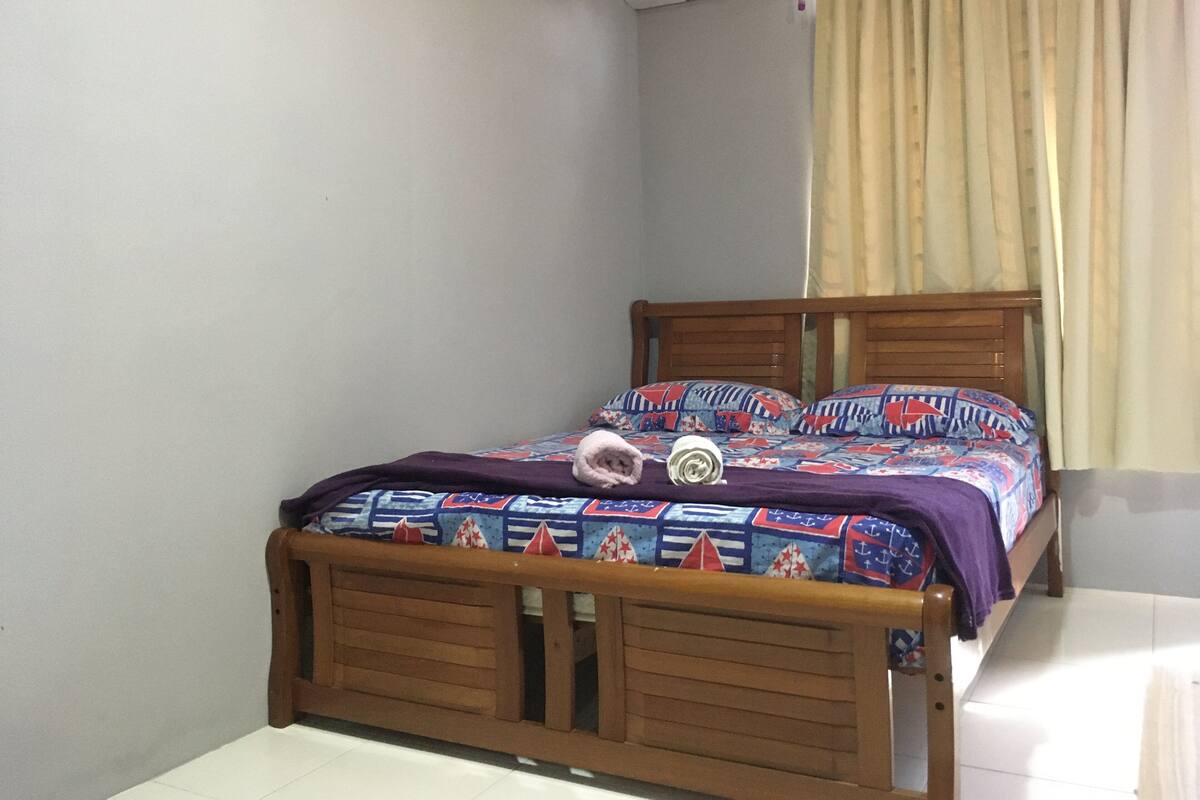 Un dormitorio con cama de madera, colcha estampada y ventana con cortinas.