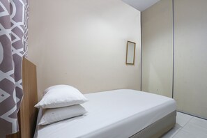 A single bed with white bedding, a wooden headboard, and a plain wall with a small mirror.
