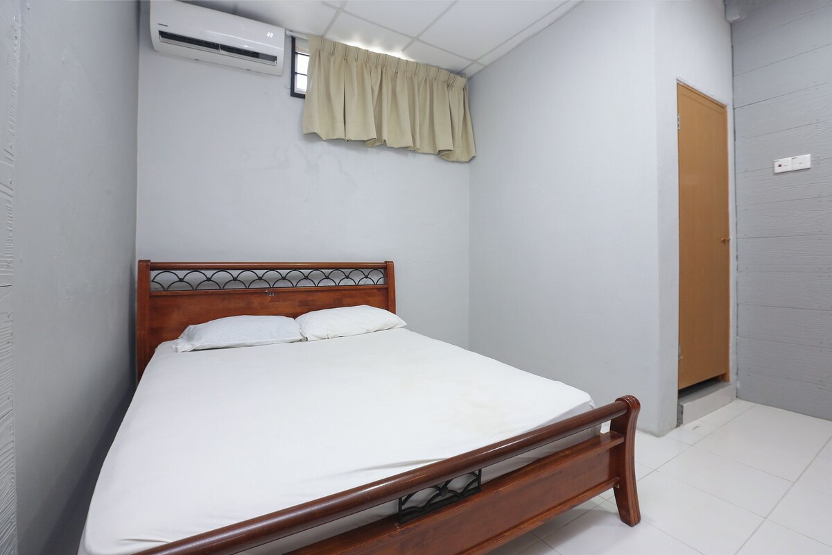 A single bed with a wooden frame and white bedding, an air conditioner, a beige curtain, and a wooden door.