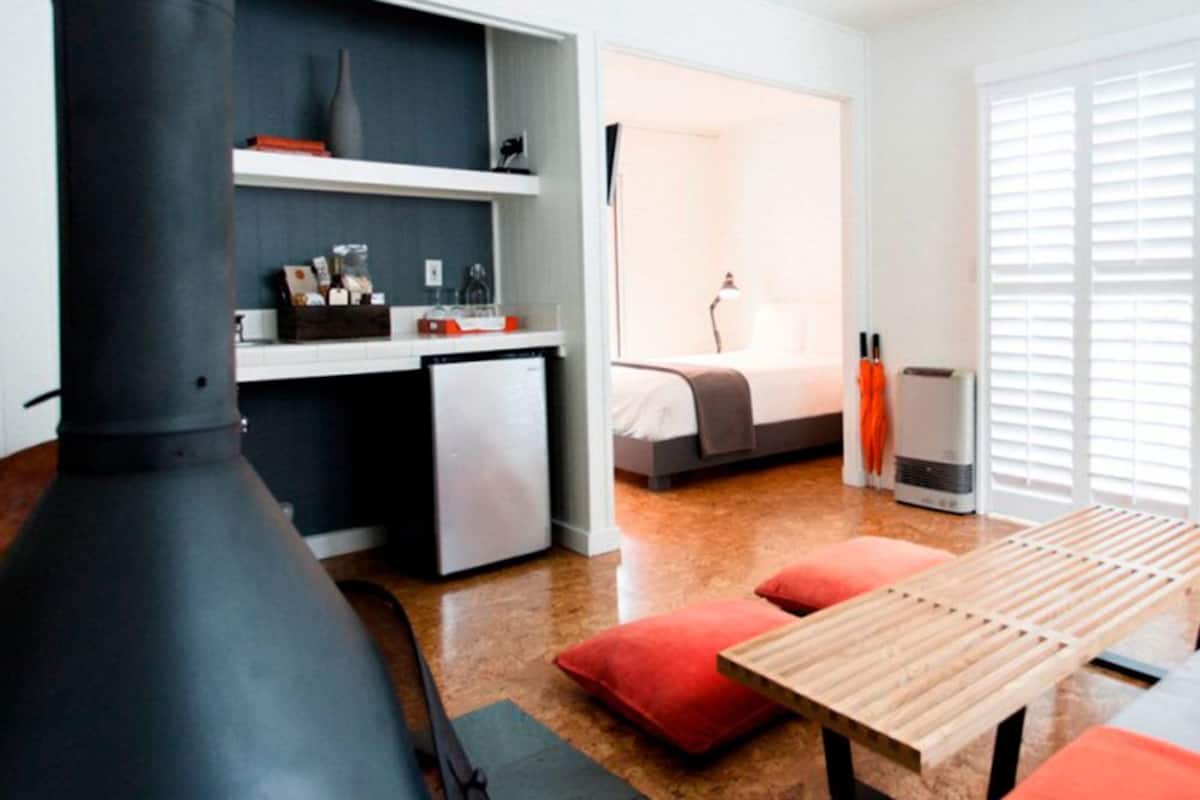 A modern hotel room with a kitchenette, a bed, a table, and a seating area.