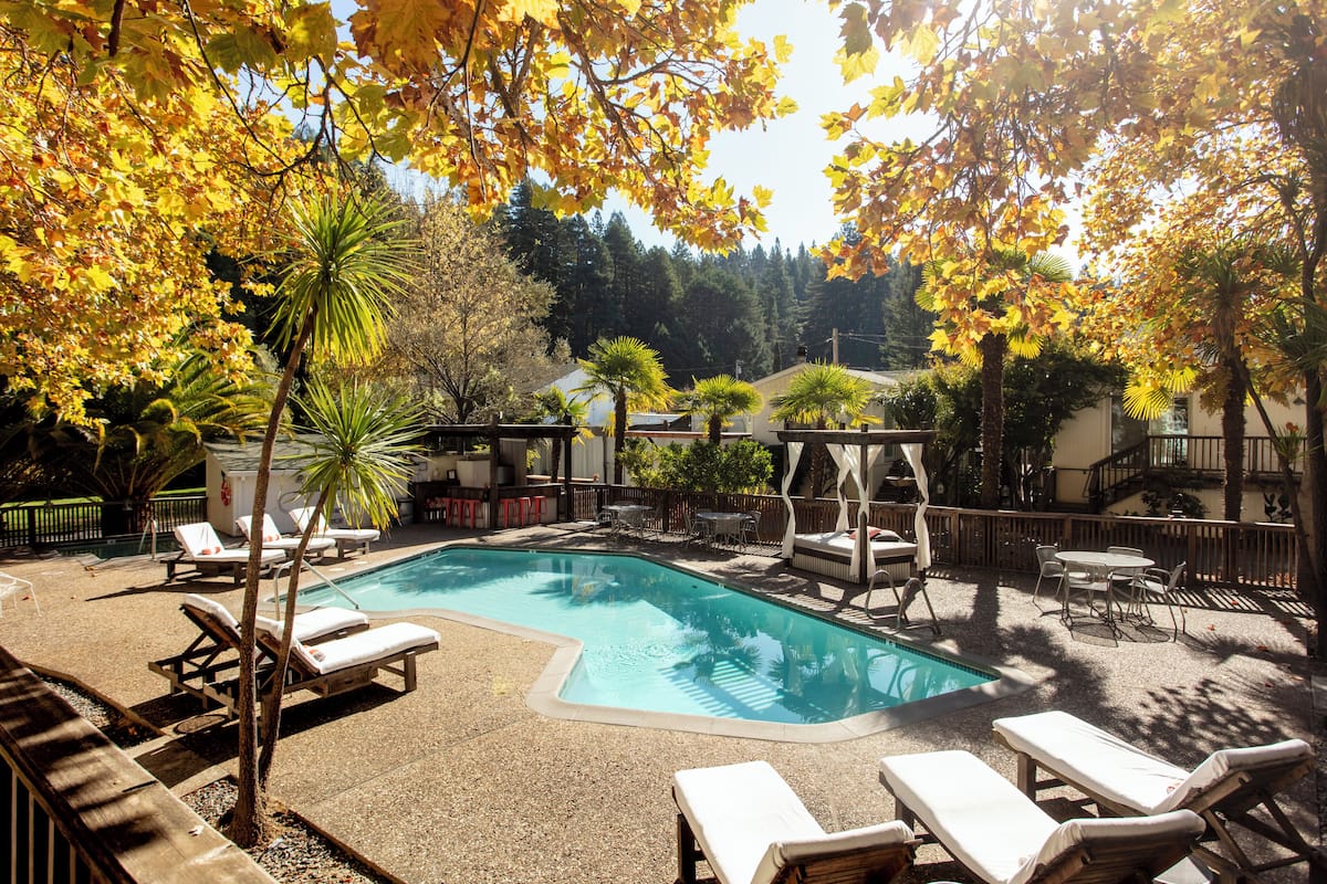 A swimming pool with lounge chairs and a gazebo, surrounded by trees and a building in the background.