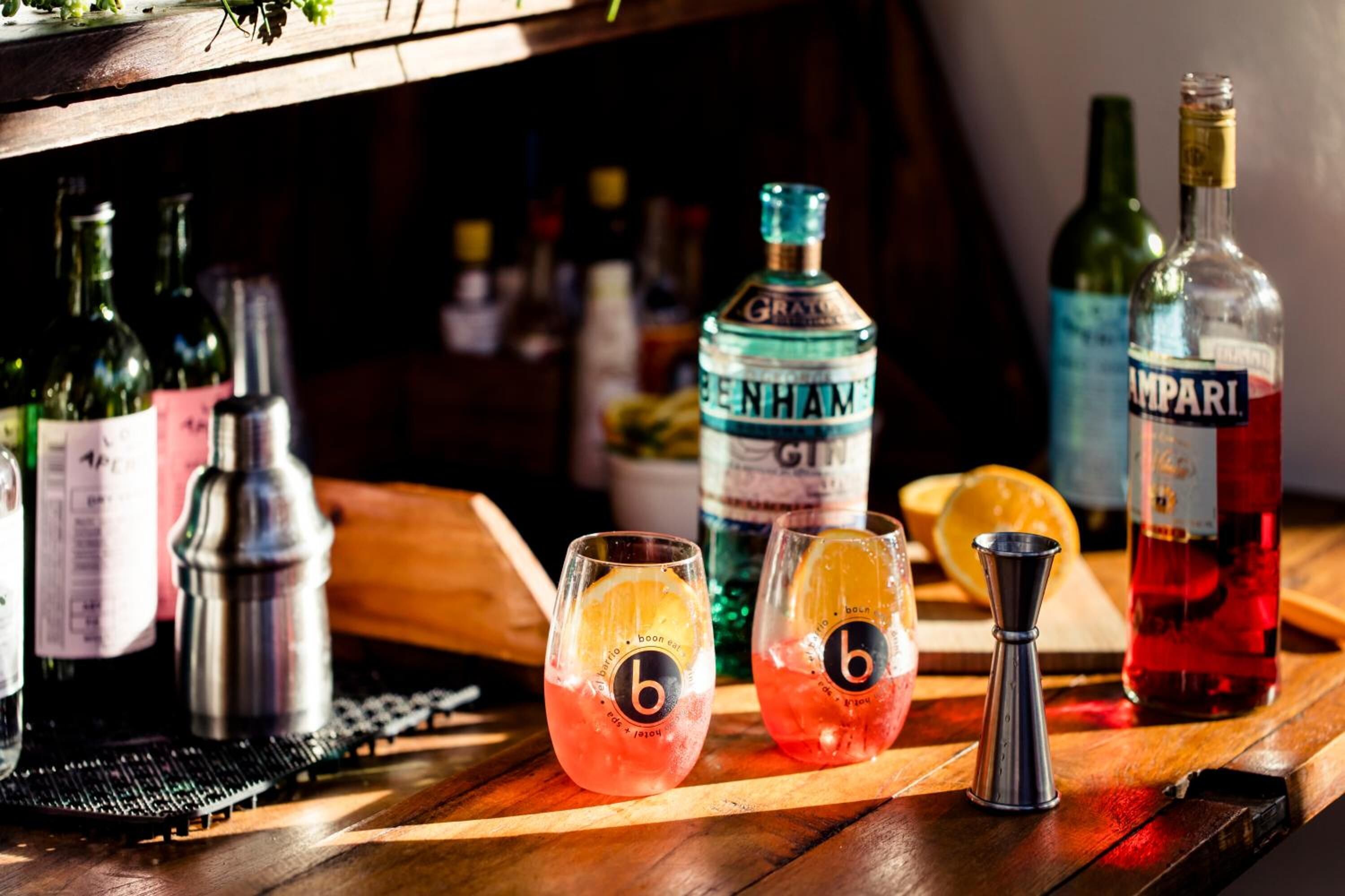 Baaritiski, jonka päällä on Benham'sin ja Amparin pulloja, kaksi lasia, joissa on «b»-logo, ja cocktail-sekoitin puupinnalla.