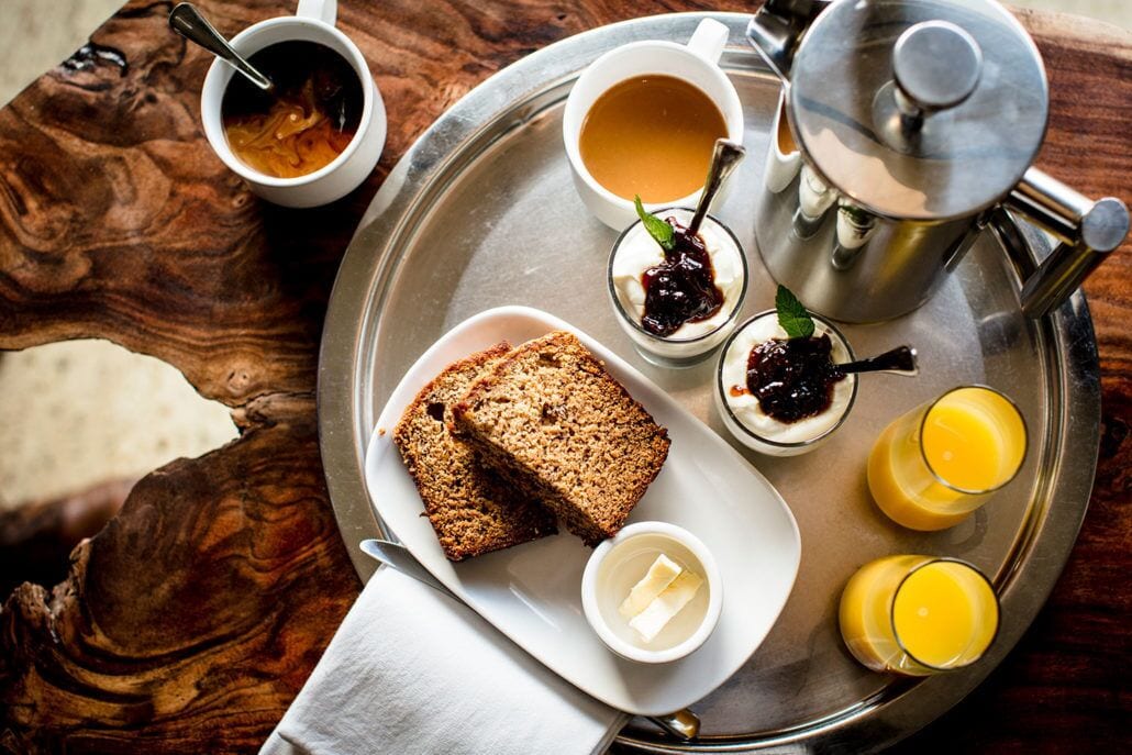 Un plateau contenant des aliments pour le petit-déjeuner, notamment des toasts, de la confiture, du beurre, du thé et du jus d’orange.