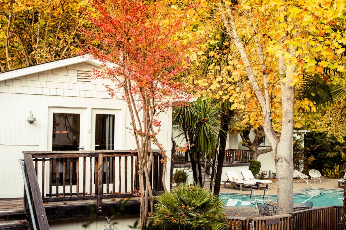 A white building with a deck, a pool, and lounge chairs.