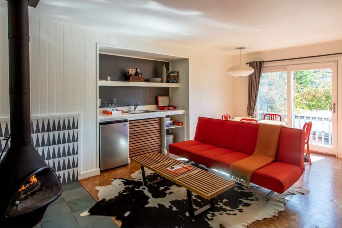 A compact living space with a kitchenette, a red sofa, a wooden table, and a black and white cowhide rug.