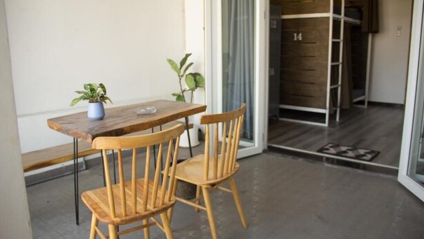 Una pequeña mesa de madera con dos sillas, una planta en maceta y una puerta corrediza de vidrio que da a una habitación con una escalera de madera.
