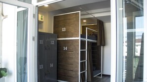 Habitación de hotel con literas, un armario con compartimentos numerados y un ventanal de vidrio que da a un balcón.