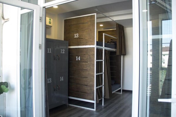 Habitación de hotel con literas, un armario con compartimentos numerados y un ventanal de vidrio que da a un balcón.