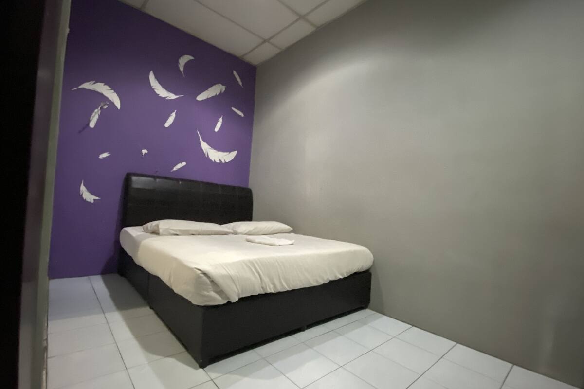 A bedroom with a bed, purple walls, and white tiles.