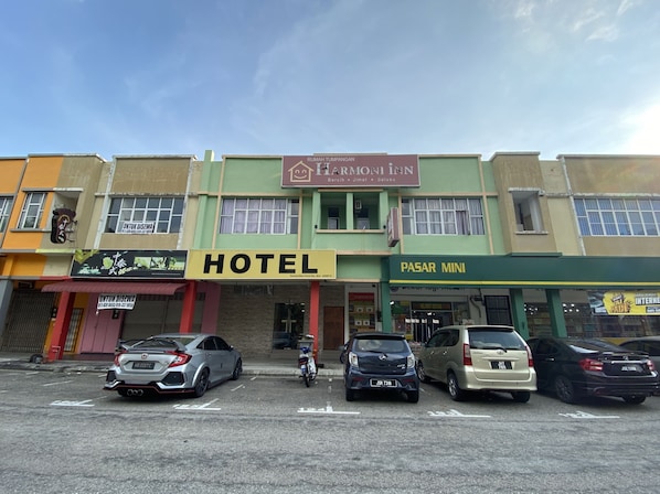 A hotel with a prominent sign, a parking lot with several cars, and adjacent buildings with various signs.