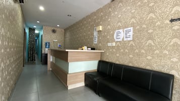 A reception area with a wooden desk, black leather couch, patterned wallpaper, and a hallway leading to another room.