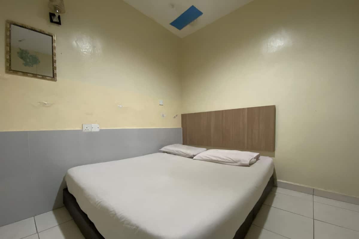 A single bed with a wooden headboard in a room with cream-colored walls and a tiled floor.