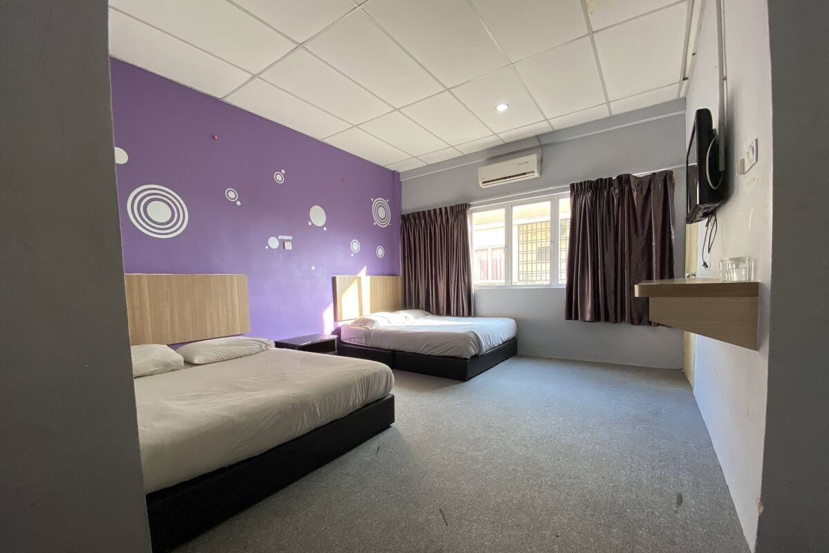 A hotel room with two beds, a built-in desk, a window with curtains, and a wall-mounted TV.