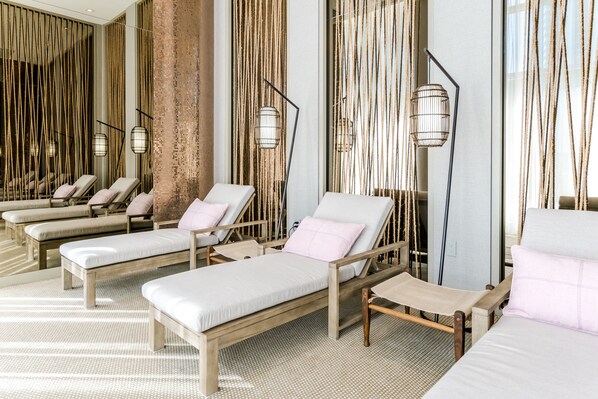 Un cuarto de spa con tumbonas de madera, un espejo grande y una lámpara de pie.
