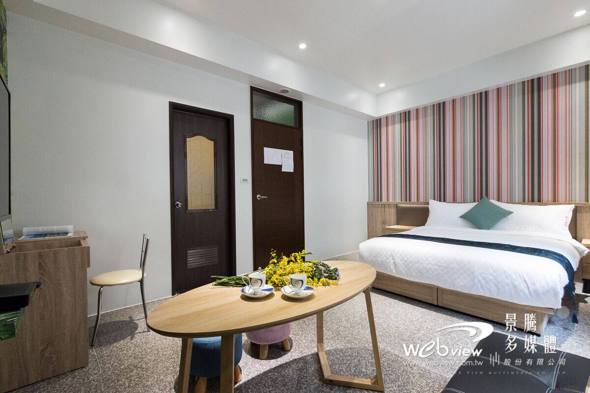 A hotel room with a bed, a desk, a chair, and a table with flowers.