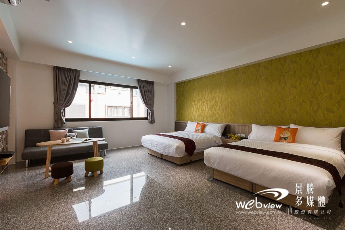 A modern hotel room with a large bed, a sofa, a small table, and a window with curtains.