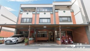A multi-story building with a covered entrance, a white car parked in front, and a motorcycle inside. - Play Inn (Dongshan)