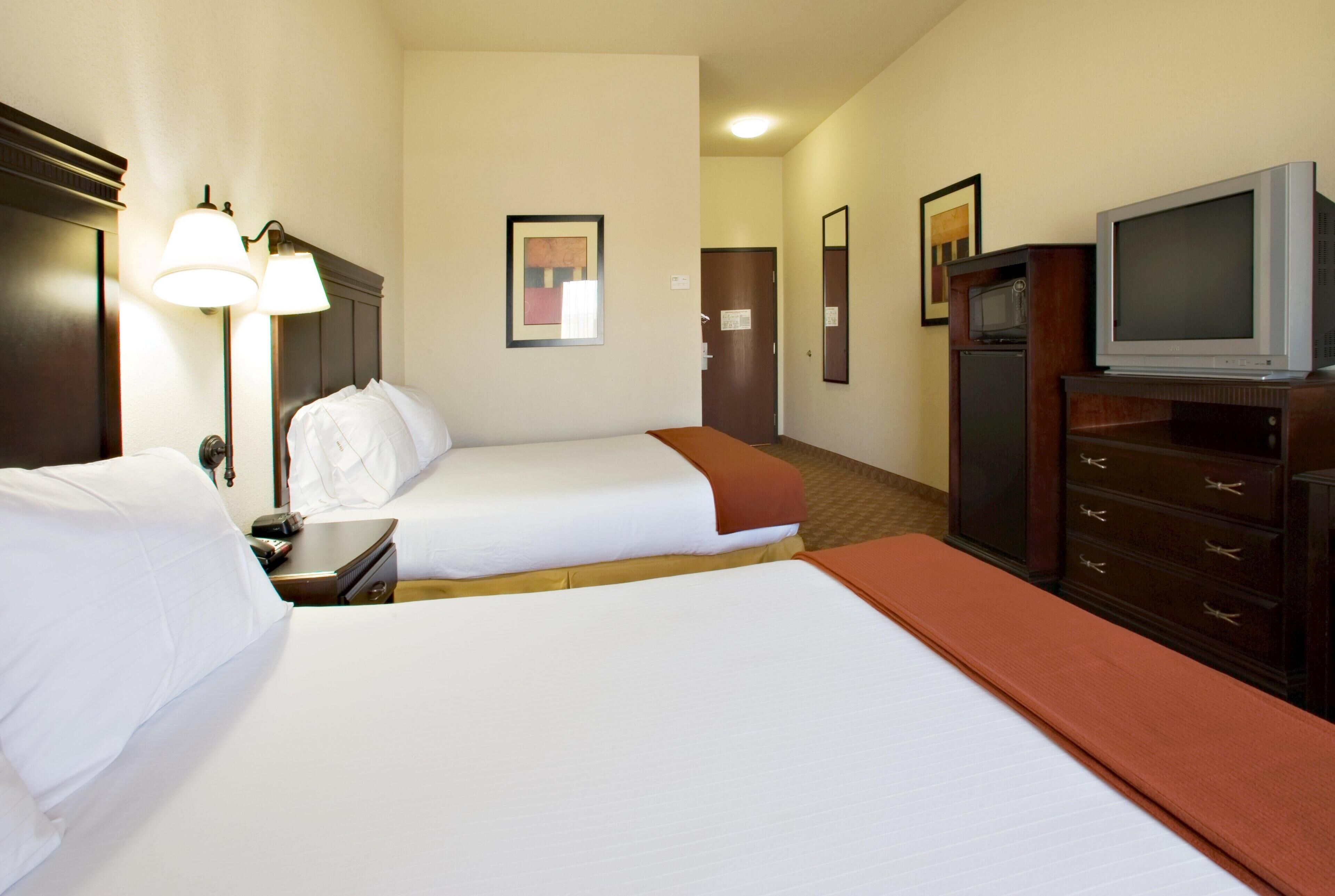 A hotel room with two beds, a television, a desk with a lamp, and a microwave.