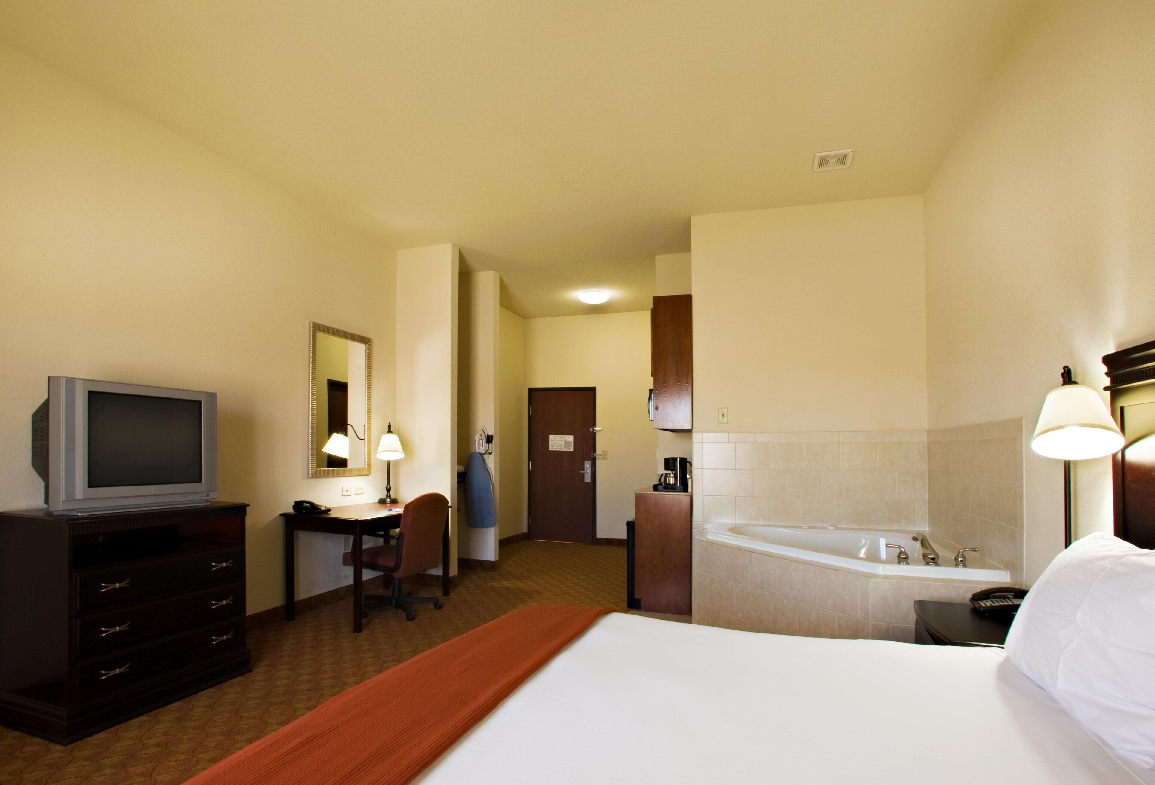 A hotel room with a bed, a desk, a television, a chair, a bathroom with a bathtub, and a mirror.