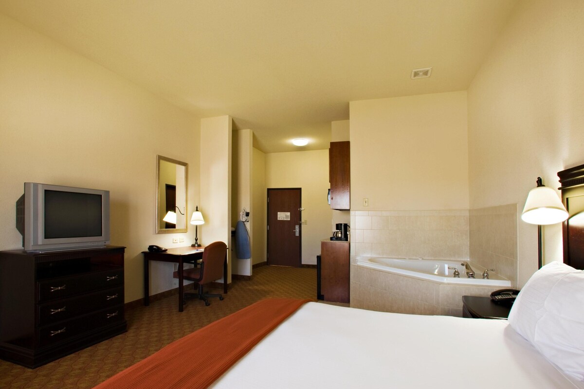 Habitación de hotel con cama, escritorio, televisor, silla, baño con bañera y espejo.