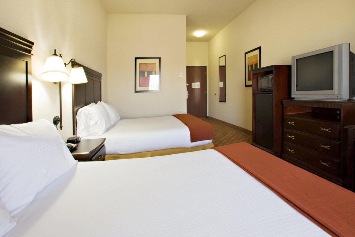 Una habitación de hotel con dos camas, televisión, escritorio con lámpara y microondas.