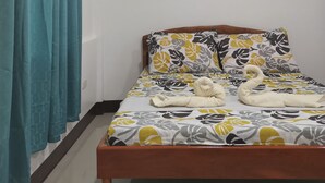 Une chambre à coucher avec un lit, des rideaux de couleur turquoise, un tableau représentant des motifs floraux et un luminaire au plafond.