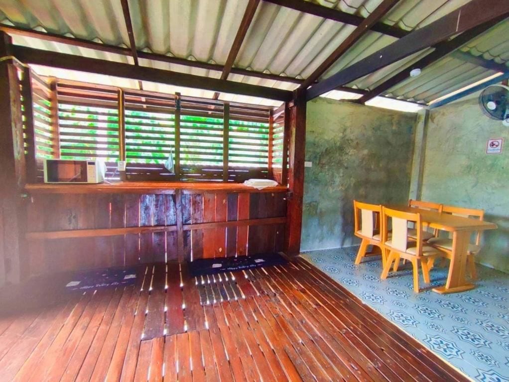 Una habitación con suelo de madera, una ventana con persianas, una mesa y sillas, y un ventilador fijado a la pared.