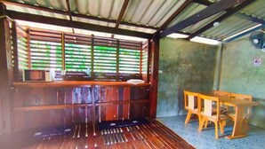 A room with a wooden floor, a window with blinds, a table and chairs, and a wall-mounted fan. - BaanThai Nakano Homestay (Mae Rim)