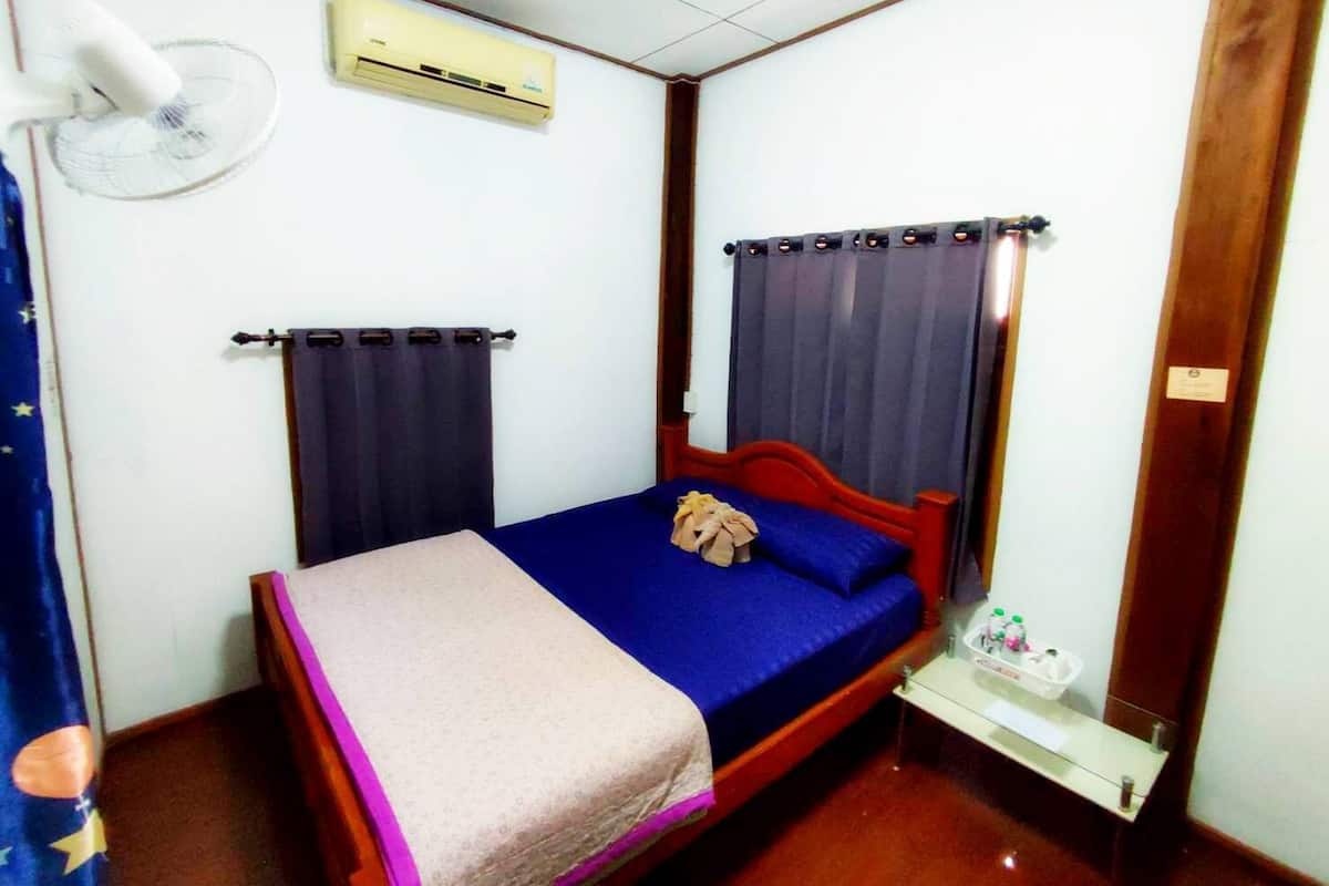 A small, single-bed room with a wooden headboard, a bedside table with a lamp, and an air conditioning unit mounted on the wall.