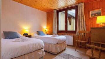 Une chambre avec deux lits, des murs en bois, une fenêtre avec des rideaux, une lampe et une chaise.