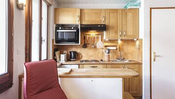 Une cuisine compacte avec des meubles en bois, un four encastré et un petit îlot central agrémenté d’un tabouret.