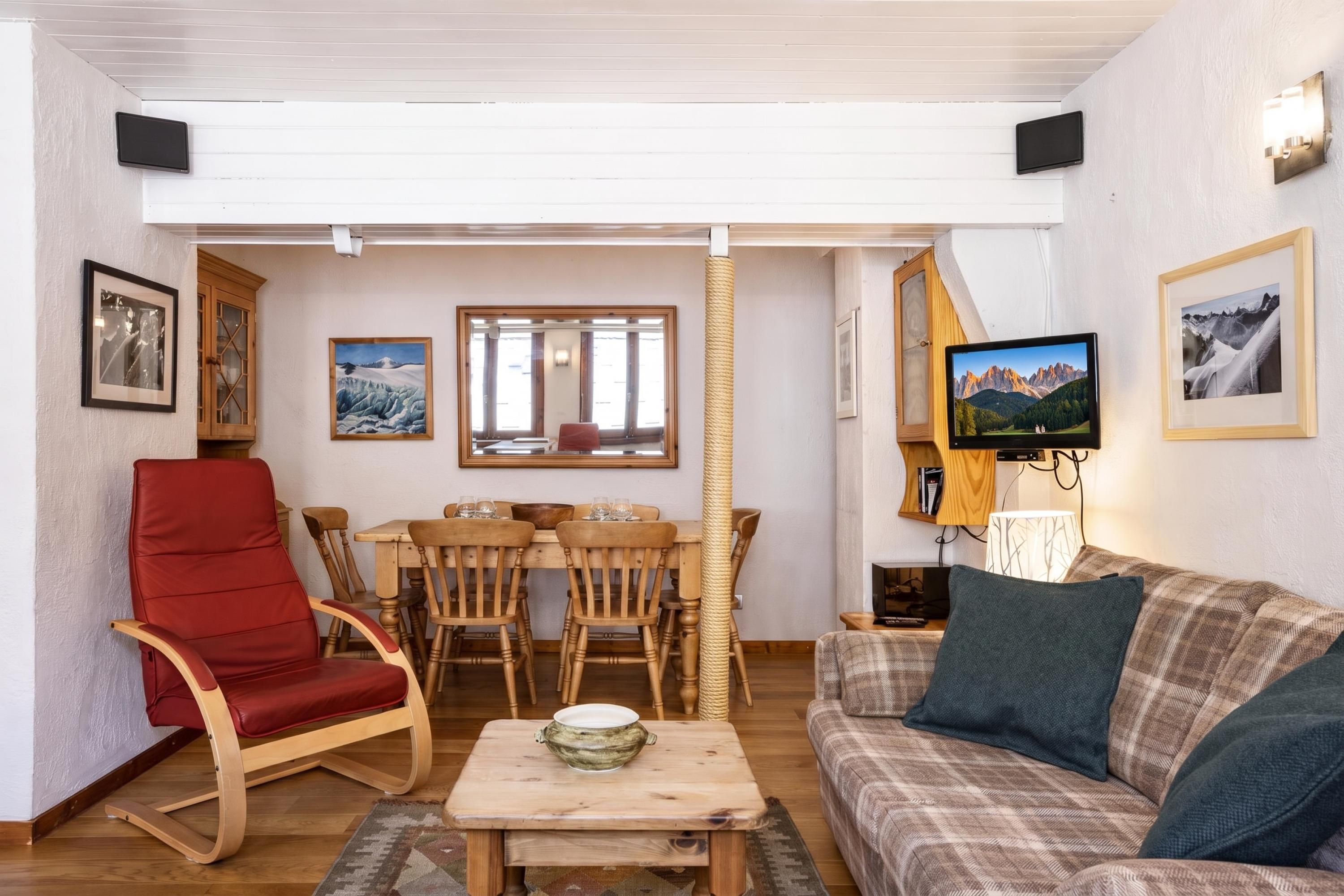 Un salon chaleureux avec un fauteuil rouge, une table à manger en bois avec des chaises, un canapé et un téléviseur.
