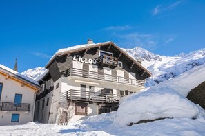 A chalet with a balcony, surrounded by snow and mountains.