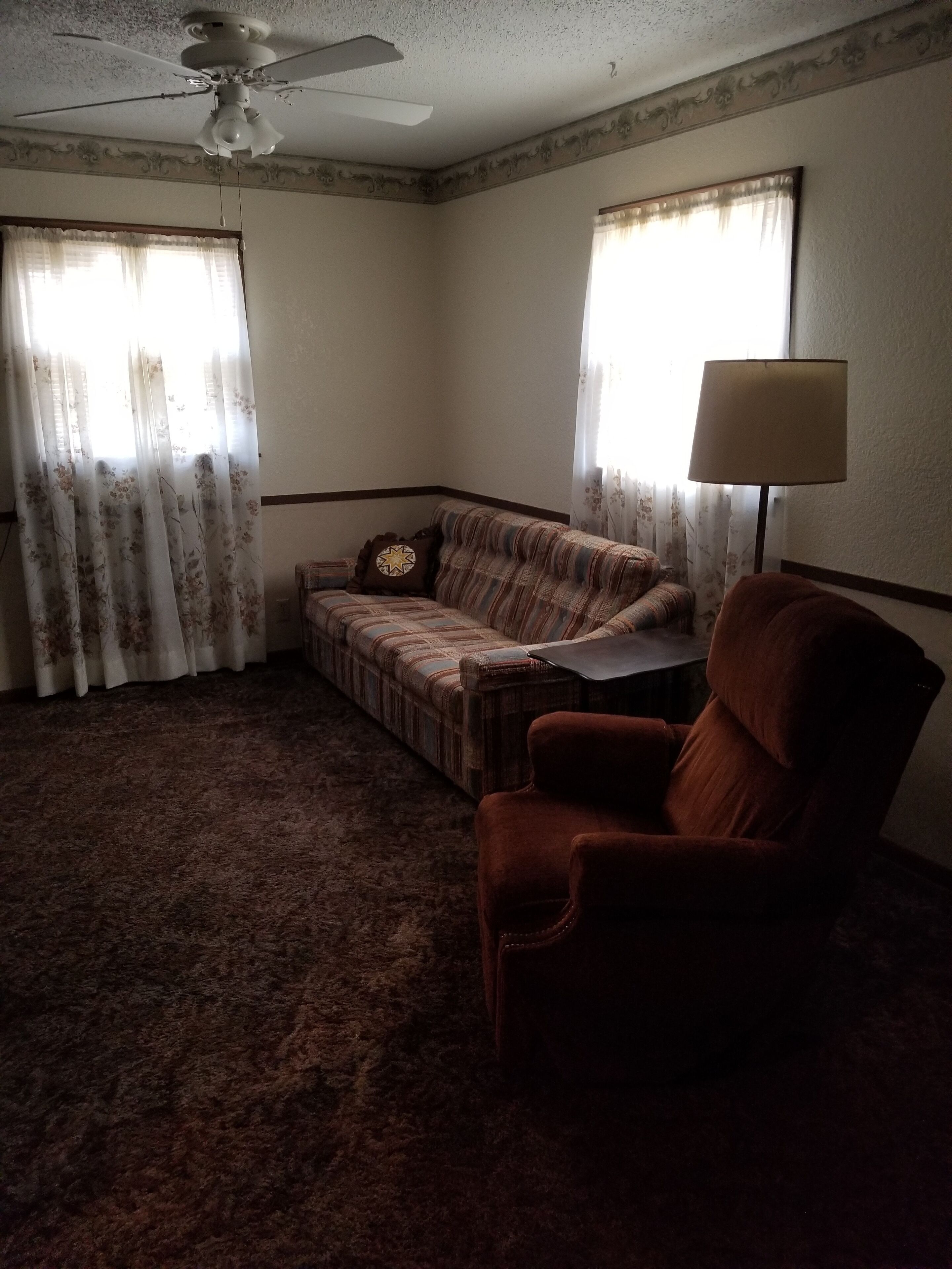 A living room with a ceiling fan, a sofa, a chair, and a lamp.