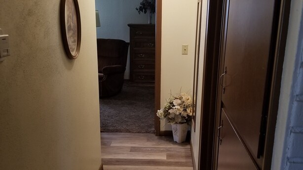 A narrow hallway with wooden flooring, a framed picture on the left wall, a potted plant, and a door leading to another room. - Grandma's house in the heart of Goddard (Goddard)