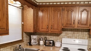 A kitchen with wooden cabinets, a white stove, a sink, and a coffee maker. - Grandma's house in the heart of Goddard (Goddard)
