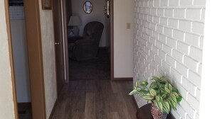 A hallway with a wooden floor, a potted plant, and a wall clock. - Grandma's house in the heart of Goddard (Goddard)