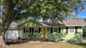 A green single-story house with a front porch, a garage, and a large tree in the yard. - Grandma's house in the heart of Goddard (Goddard)