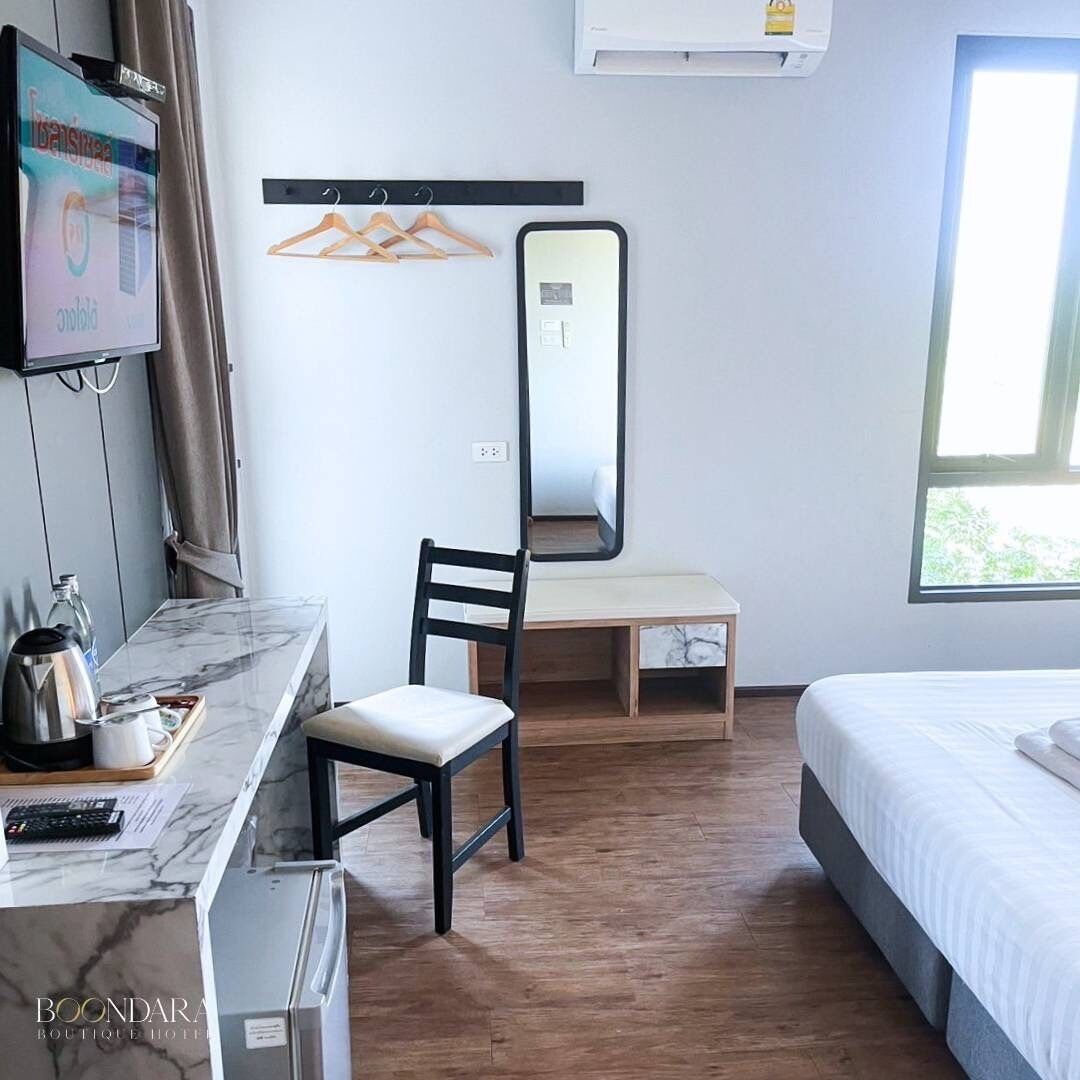 A hotel room with a marble desk, a chair, a bed, a mirror, a TV, and a window.