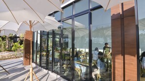 Een terras met glazen wanden, parasols en een modern architectonisch ontwerp.